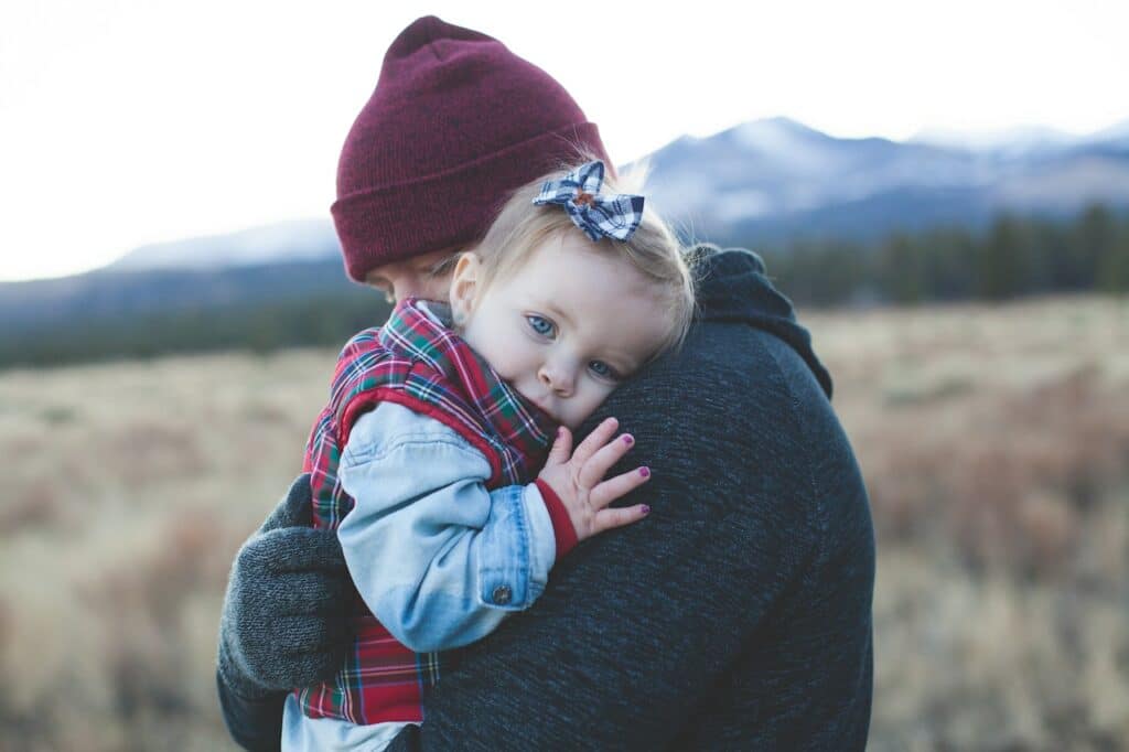 Stressed parent in need of perinatal therapy sessions holds baby in field.