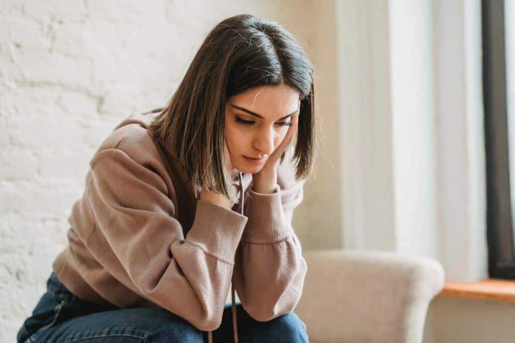 Sad Woman at chair with Postpartum depression holds her head and leans over. 