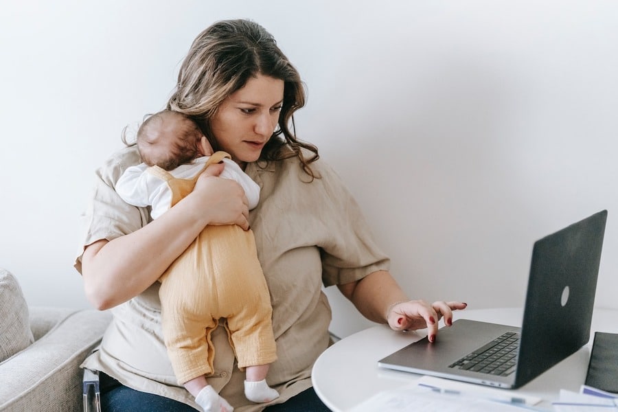 A mother is holding her baby while doing some work on her computer
