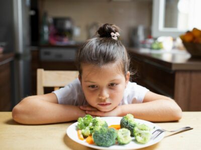 an image of a little girl refusing to eat healthy food and showing signs of picky eating