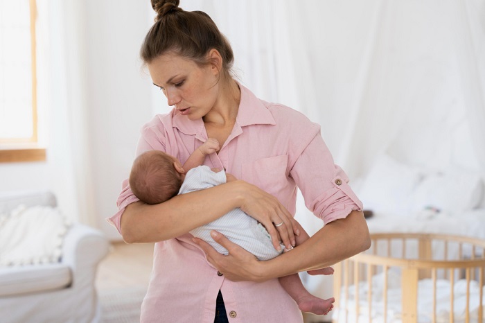 A woman holding her newborn baby with a concerned expression on her face, representing the challenges of postpartum anxiety